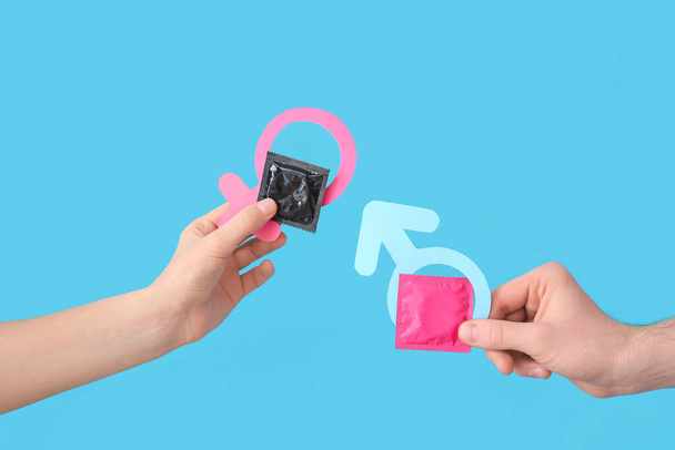 Handen met condooms en symbolen van vrouw en man op kleur achtergrond - Foto, afbeelding