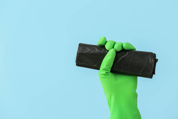 Hand in rubber glove with roll of garbage bag on color background - Φωτογραφία, εικόνα