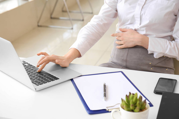 Zwangere zakenvrouw werkt met laptop op kantoor - Foto, afbeelding