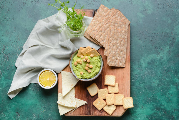 Bowl with tasty green pea hummus, chickpeas and crackers on color background - Photo, Image