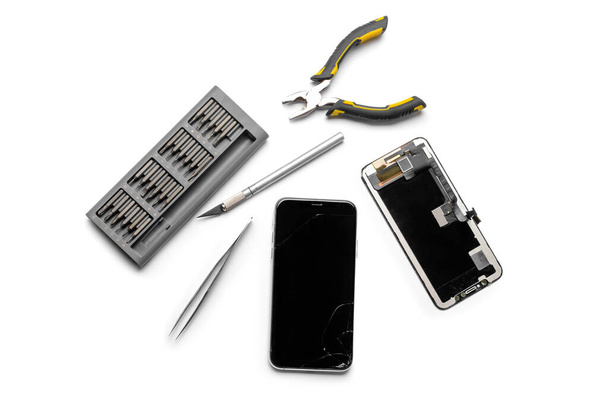 Gedemonteerde mobiele telefoon met technicus gereedschap op witte achtergrond - Foto, afbeelding