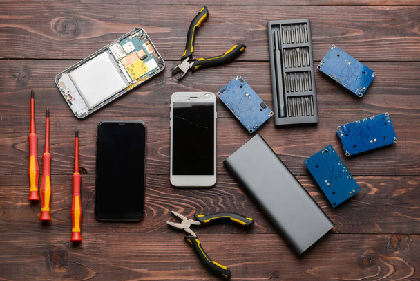 Damaged mobile phones with technician tools on wooden background - Foto, imagen