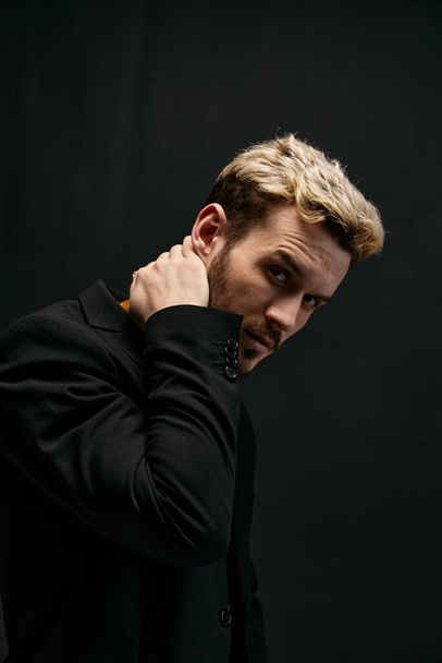  man model in a sweater and coat holds his hand behind his head on a dark background  - Photo, Image
