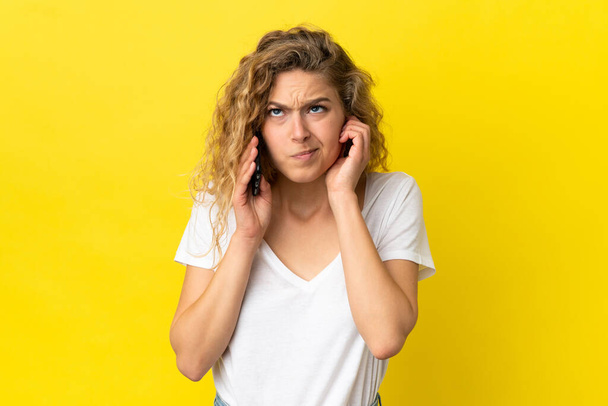 Young blonde woman using mobile phone isolated on yellow background frustrated and covering ears - Foto, immagini