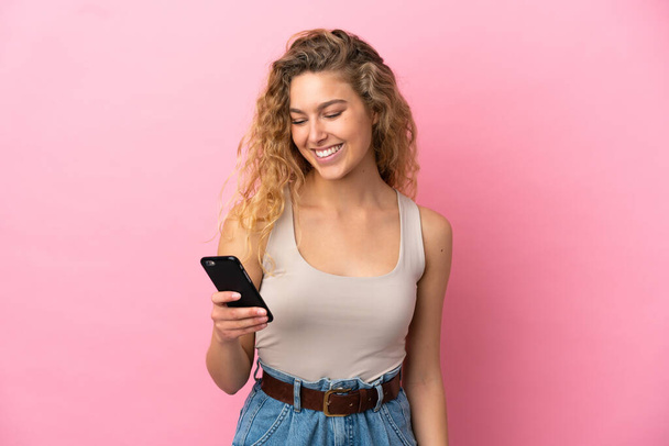 ピンクの背景に隔離された若いブロンドの女性携帯電話でメッセージや電子メールを送信 - 写真・画像
