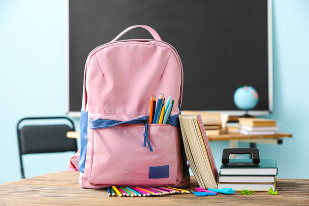 School backpack with stationery on table in classroom - Foto, Imagen