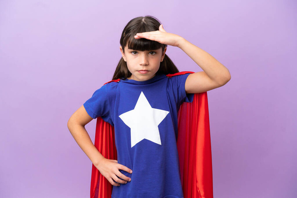 Little kid isolated on purple background in superhero costume and showing something - Foto, Imagen