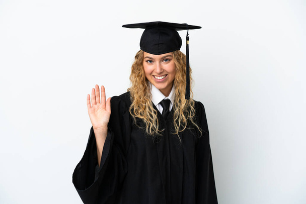 Νεαρός απόφοιτος πανεπιστημίου απομονώνονται σε λευκό φόντο χαιρετισμό με το χέρι με ευτυχισμένη έκφραση - Φωτογραφία, εικόνα