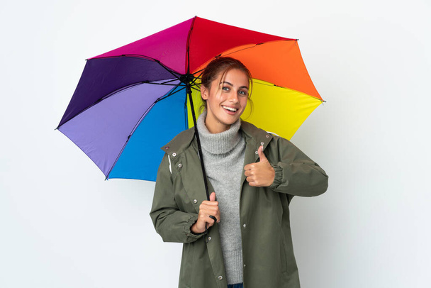 Mladá žena drží deštník izolovaný na bílém pozadí dává palce nahoru gesto - Fotografie, Obrázek