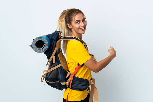 Young mountaineer woman with a big backpack isolated on white background pointing back - Photo, image