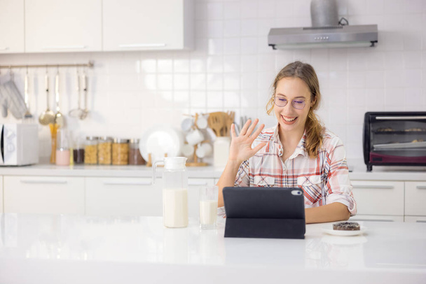 W nowoczesnej kuchni, piękna młoda kobieta używa tabletu cyfrowego jedząc zdrowe śniadanie. - Zdjęcie, obraz