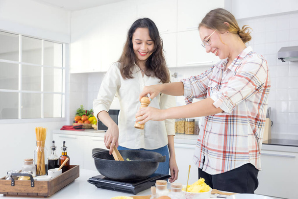 Στην κουζίνα, δύο χαρούμενες δίδυμες αδερφές ετοιμάζουν μακαρόνια για μεσημεριανό.. - Φωτογραφία, εικόνα