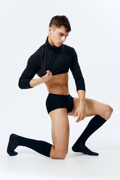 брюнетка парень с атлетическим телосложением преклоняет колени на светлом фоне - Фото, изображение