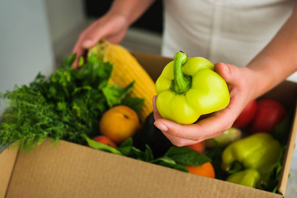 een meisje pakt een pakje uit in een winkel met groenten en fruit. online levering van goederen aan uw huis. groenten in een doos close-up - Foto, afbeelding