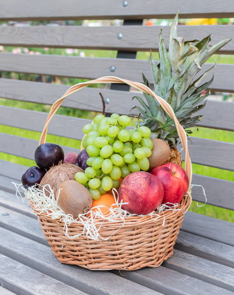 Cesta redonda de mimbre llena de frutas frescas y bayas se encuentra en un banco de madera - Foto, Imagen