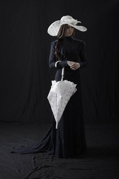 A girl in an old dress and hat stands on a dark background and is sad - Photo, Image