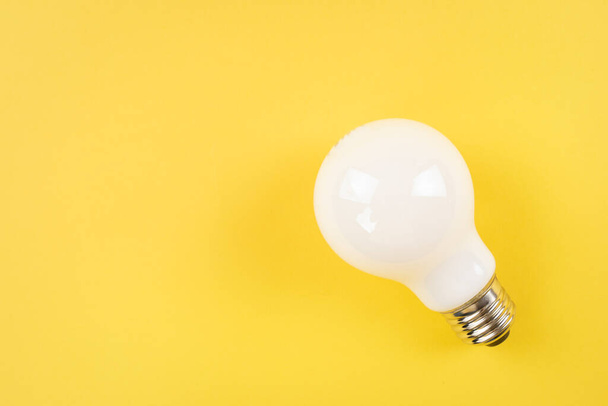 Opaque white light bulb on yellow background - Fotó, kép