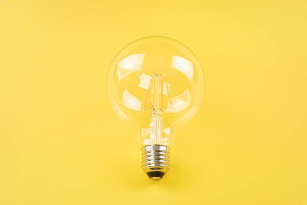 Transparent light bulb on yellow background - Foto, afbeelding