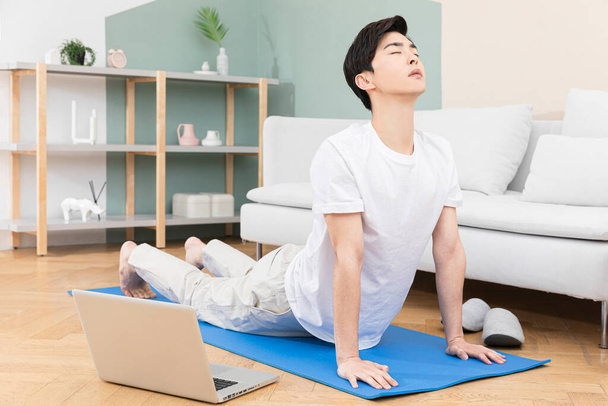 Asian male young man meditating with a laptop sitting on a yoga mat - Foto, afbeelding
