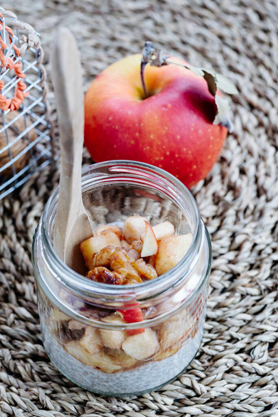 A closeup of fresh delicious sweet yogurt with sliced apples in a glass jar with a wooden spoon - Valokuva, kuva
