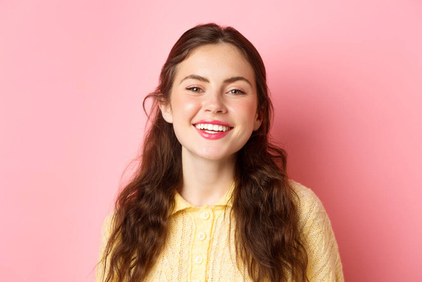Close up of happy carefree lady laughing and smiling, looking pleased and relaxed at camera, standing against pink background - Zdjęcie, obraz