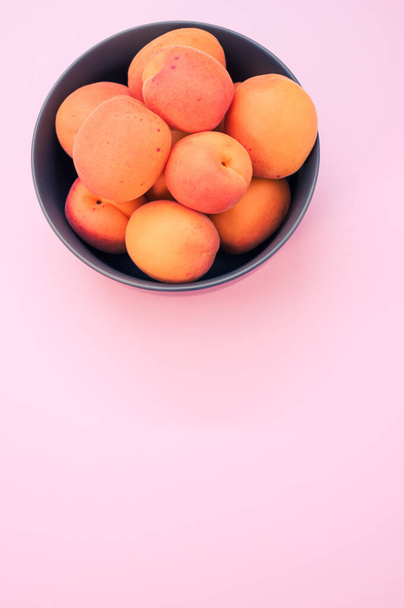 A vertical shot of fresh apricots on a bowl isolated on light pink background with copy space - Photo, Image