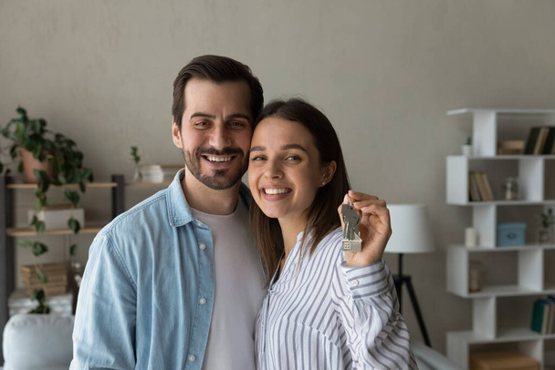 Young couple bought new house showing keys at camera - Foto, afbeelding