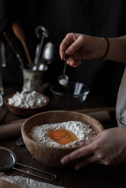 A vertical shot of female hands adding eggs to dough in a wooden bowl - Valokuva, kuva