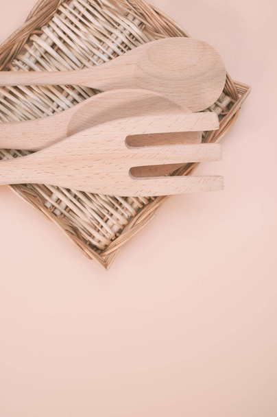 A vertical shot of wooden spoon and fork on a flat wicker basket isolated on light cream background - Foto, Imagem