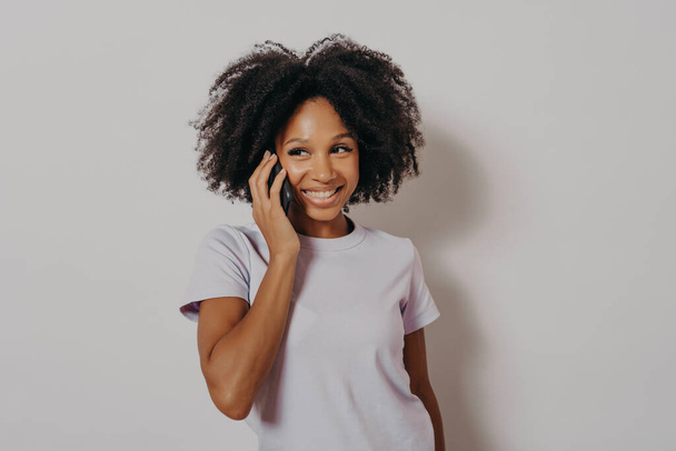 Studio portrait of cheerful dark skinned woman enjoying conversation on mobile phone - Photo, image
