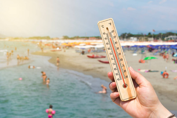 Женщина держит термометр перед переполненным итальянским пляжем - Фото, изображение