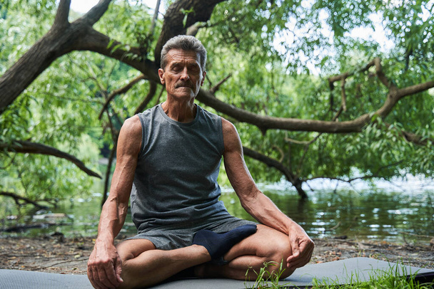 Senior man keeping eyes closed and meditating at the cozy forest or park - Foto, immagini