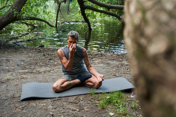 Senior man keeping eyes closed and meditating at the cozy forest or park - Foto, imagen