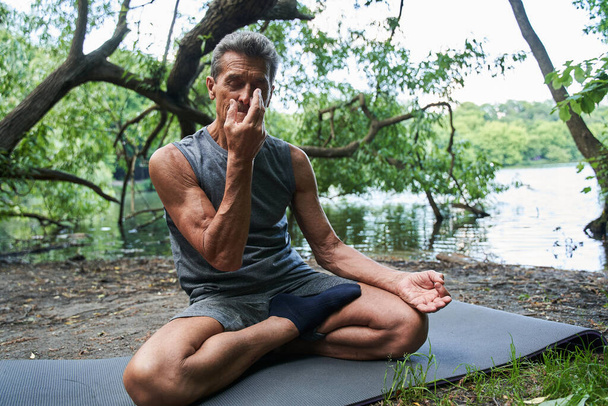 Hombre haciendo ejercicio respiratorio mientras cierra una fosa nasal con un dedo durante la sesión - Foto, imagen