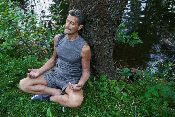 Retirement male with crossed legs and closed eyes meditating at the park - Foto, imagen