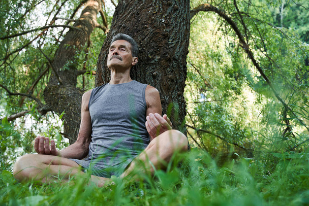 Man keeping eyes closed while sitting in yoga position at the forest - 写真・画像