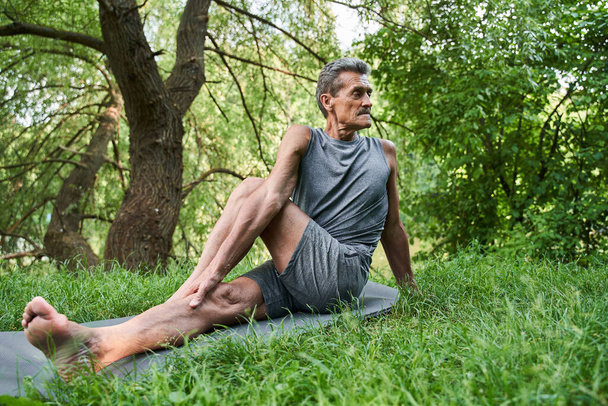Man making exercises on the stretching legs and looking aside while sitting - Foto, afbeelding