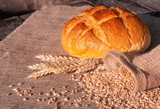 Bochníky pšeničného chleba a špičky pšenice leží na dřevěném stole potaženém lopatkou - Fotografie, Obrázek