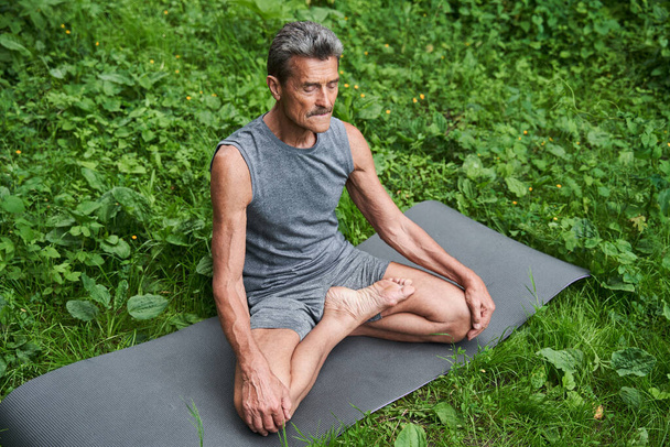 Caucasian mature man meditates while practicing yoga at the mat - Fotografie, Obrázek