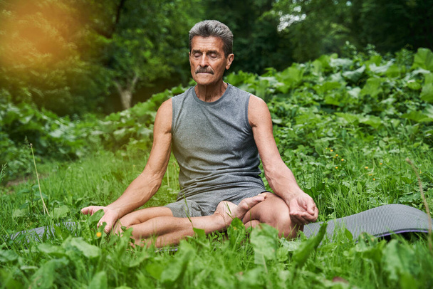 Man practicing yoga and doing ardha padmasana exercise while sitting on lotus position - Фото, изображение