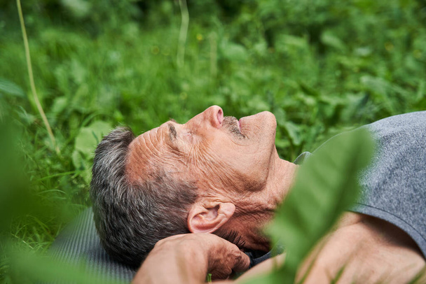 Mature man doing relaxing yoga pose while laying on the mat at the nature - Foto, afbeelding