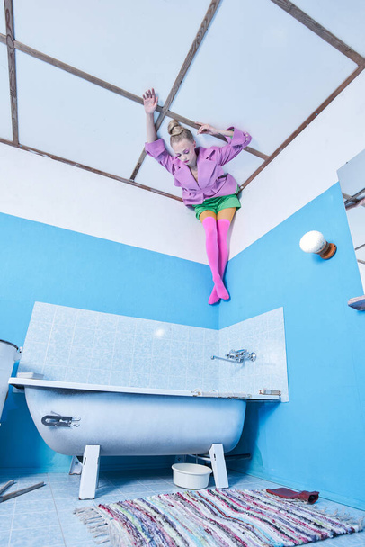 Girl wearing bright clothes laying at the ceiling head over heels at the bathroom - Fotografie, Obrázek