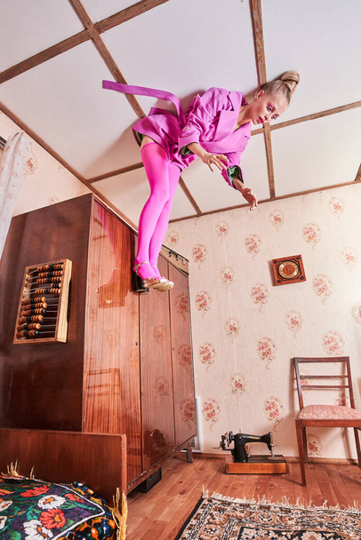 Woman in pink clothes laying at the ceiling near wardrobe while posing head over heels - Фото, зображення