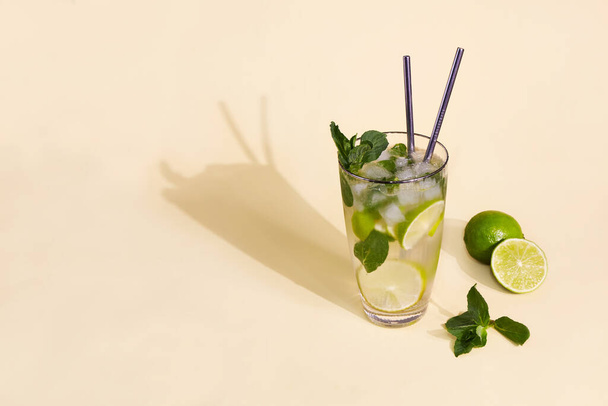 A glass with mojito on yellow background. Fresh cold refreshing summer cocktail with lime, mint and ice . - Fotó, kép