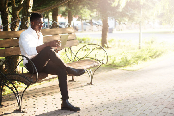 African-American businessman, working at a laptop on a park bench, freelancer. - Fotoğraf, Görsel