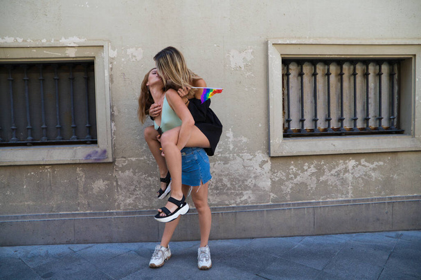 two beautiful young women on holiday. The women are lesbians and one is carrying the other. They are kissing because they are a couple. Concept of equality and diversity. - Zdjęcie, obraz