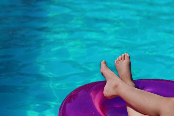 プールの背景にピンクのスイミングサークルに赤ん坊の足。コピースペース。プールによる夏のリラクゼーション. - 写真・画像