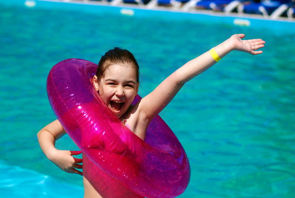 Radostná dívka se šťastně usmívá v bazénu s jasně růžovým plaveckým kruhem. Ta dívka odpočívá v bazénu. Ta dívka plave v bazénu.. - Fotografie, Obrázek