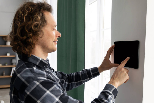 Hombre usando la tableta en la pared con la aplicación casera elegante en interiores - Foto, Imagen