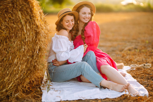 Two young woman in fashionable and stylish clothes posing near hay bales in the countryside. Fashion concept. Nature, vacation, relax and lifestyle. - Foto, immagini